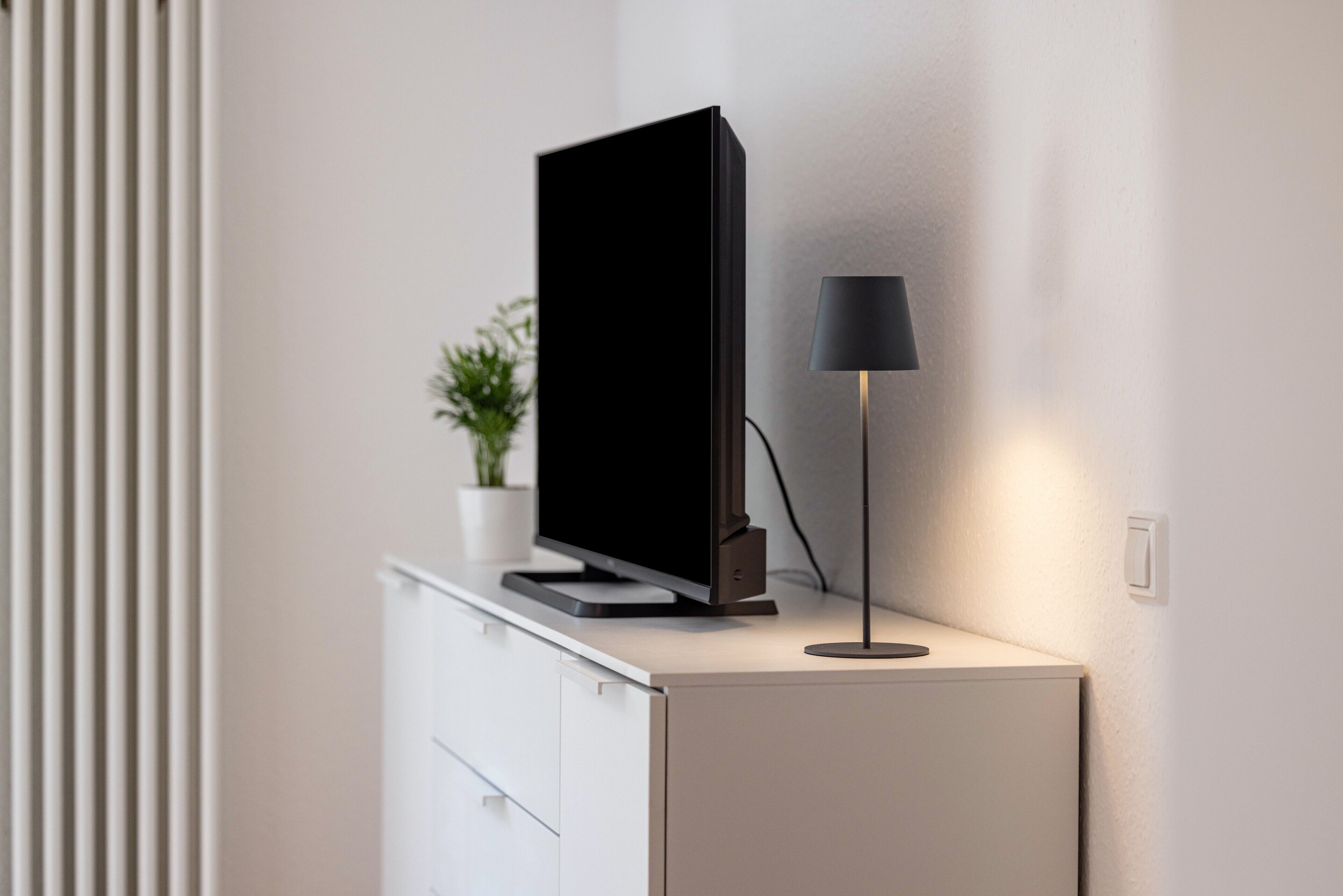 A flat-screen TV on a white cabinet with a black lamp beside it.