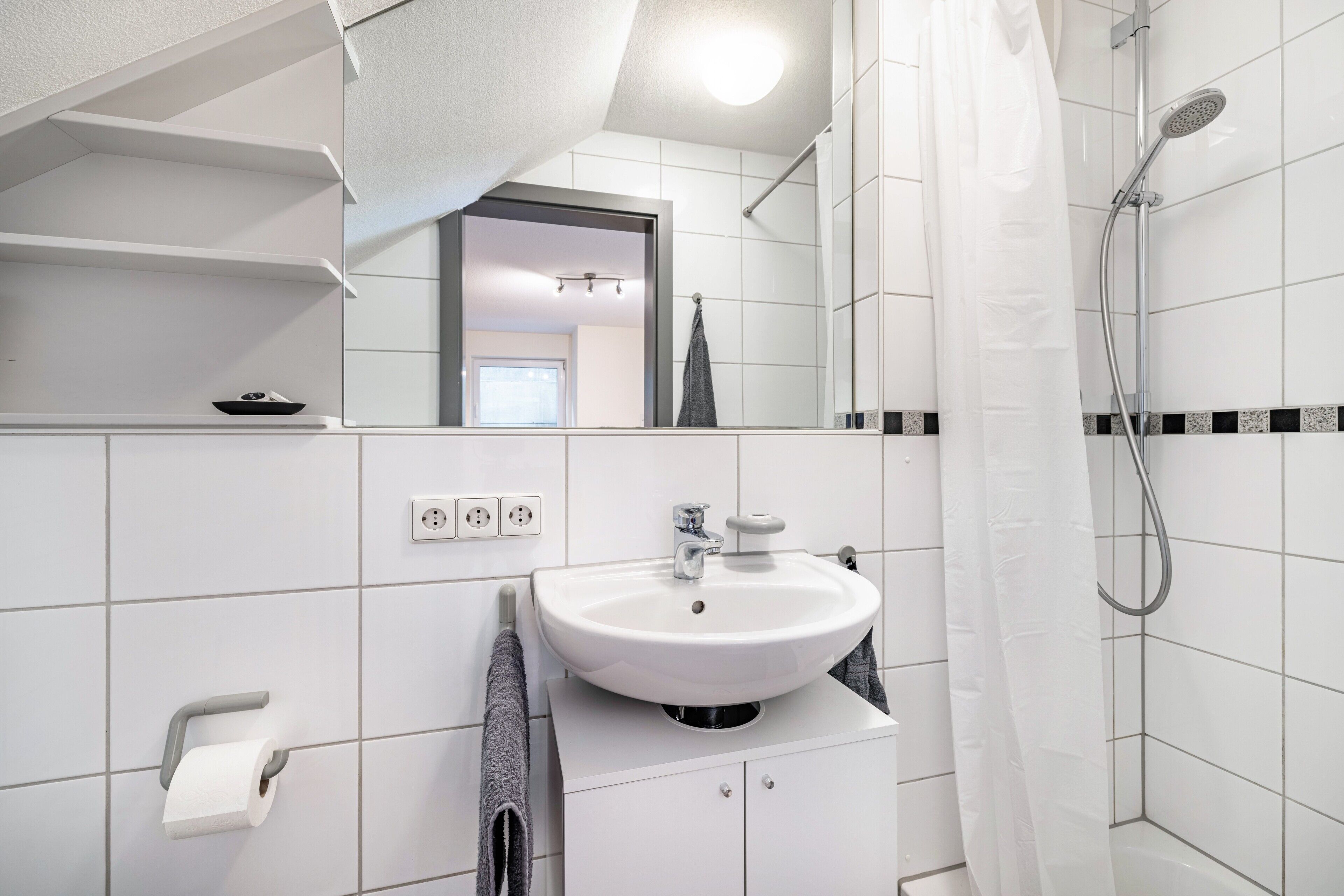 A modern bathroom with a white sink, mirror, and shower.