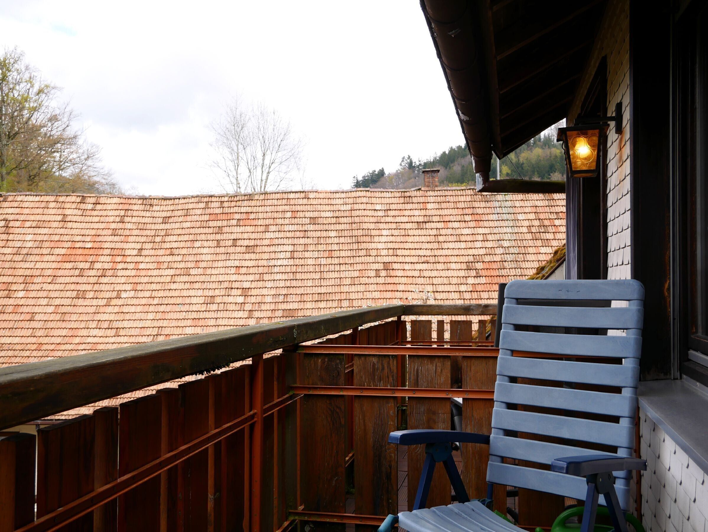 Un balcon avec une balustrade en bois, une chaise bleue et une lanterne allumée.
