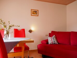 Una habitación con una mesa de comedor, sillas, un sofá, una lámpara fijada a la pared y un cuadro enmarcado.