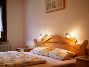 Un dormitorio con cabecera de madera, dos lámparas de noche, ropa de cama con motivos florales, un radiador y un cuadro en la pared.