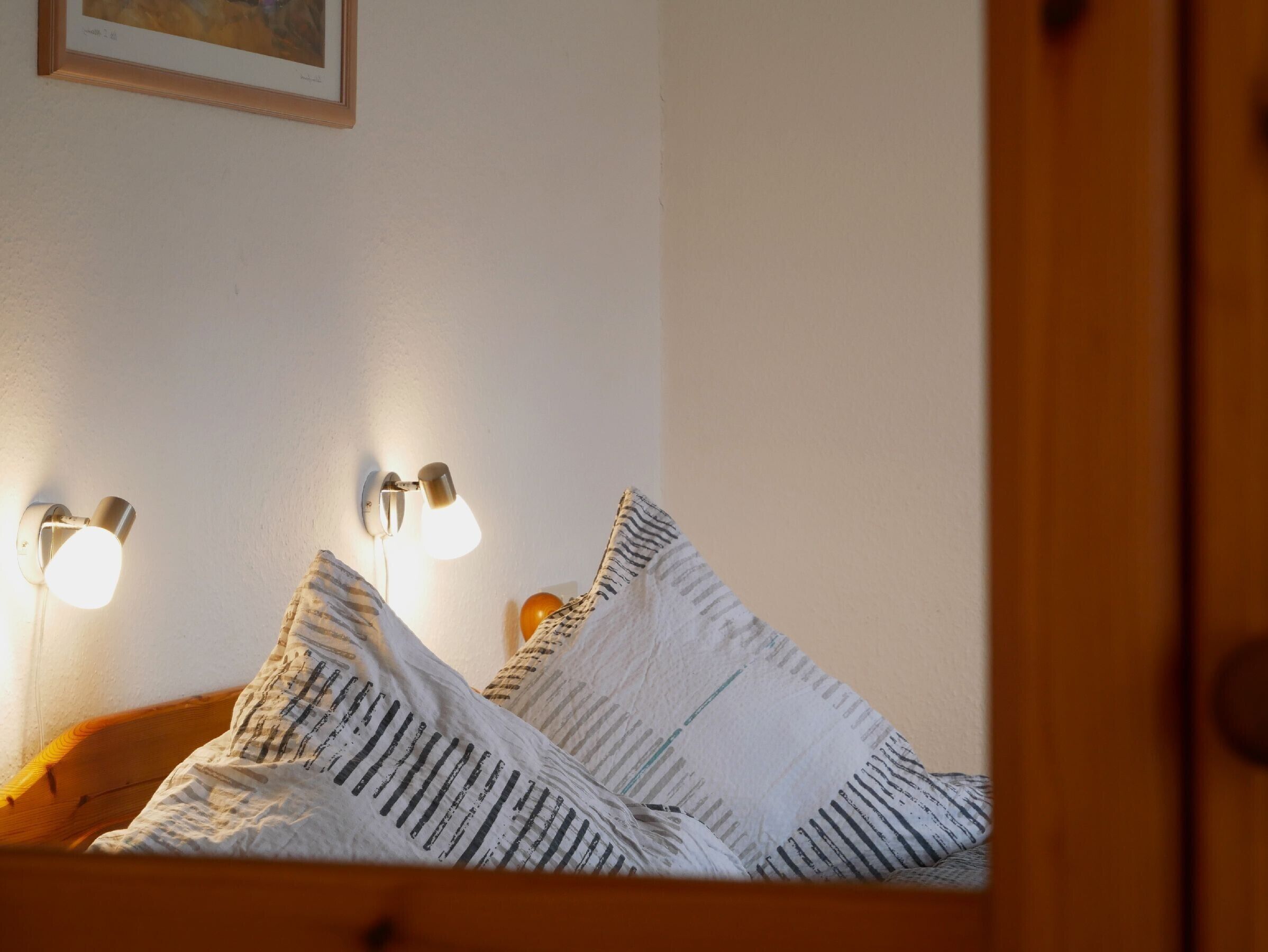 Una cama con ropa de cama a rayas, dos lámparas fijadas a la pared y un cuadro enmarcado.