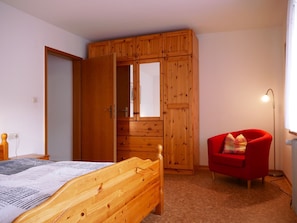 A bedroom with a wooden wardrobe, a red chair, a bed, and a floor lamp. - Apartment 'Nr 1' with Shared Garden, Balcony and Wi-Fi (Bad Peterstal-Griesbach)