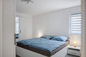 Une chambre à coucher avec un lit, des tables de chevet, une fenêtre avec des stores et une porte.