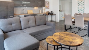 A modern kitchen with dark cabinets, a gray sofa, and a dining area with a wooden table and chairs. - Apartment 'Sonnenseite' with Private Terrace and Wi-Fi (Ihringen am Kaiserstuhl)
