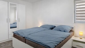 A bedroom with a bed, a wardrobe, a bedside table with a lamp, and a window with blinds. - Apartment 'Sonnenseite' with Private Terrace and Wi-Fi (Ihringen am Kaiserstuhl)