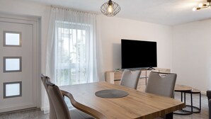 A dining area with a wooden table, chairs, a television, and a window with curtains. - Apartment 'Sonnenseite' with Private Terrace and Wi-Fi (Ihringen am Kaiserstuhl)