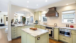 Una cocina amplia con armarios verde claro, encimera de mármol y electrodomésticos de acero inoxidable.