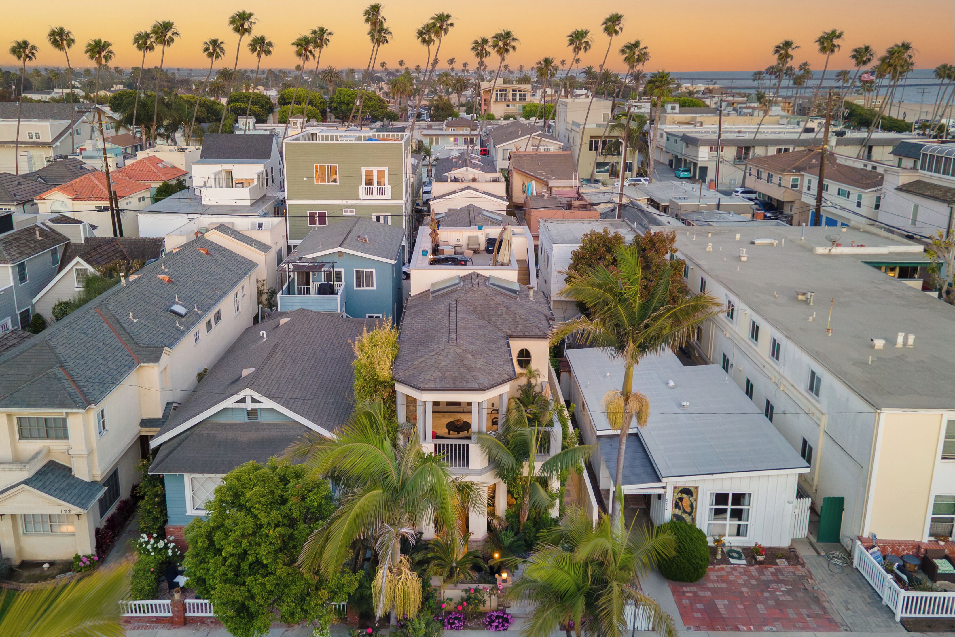 Un quartier résidentiel avec des maisons, des palmiers et une vue sur l’océan au coucher du soleil.