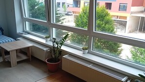 Ein Zimmer mit großen Fenstern, einem Heizkörper, einer hölzernen Bank und Topfpflanzen.