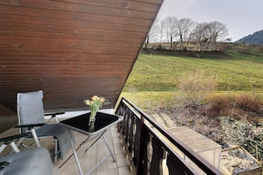 A wooden deck with a table and chairs, a vase with flowers, and a view of a grassy field and trees. - Haus Huber Holiday Apartment '2' with Covered Balcony and Wi-Fi (Wolfach)
