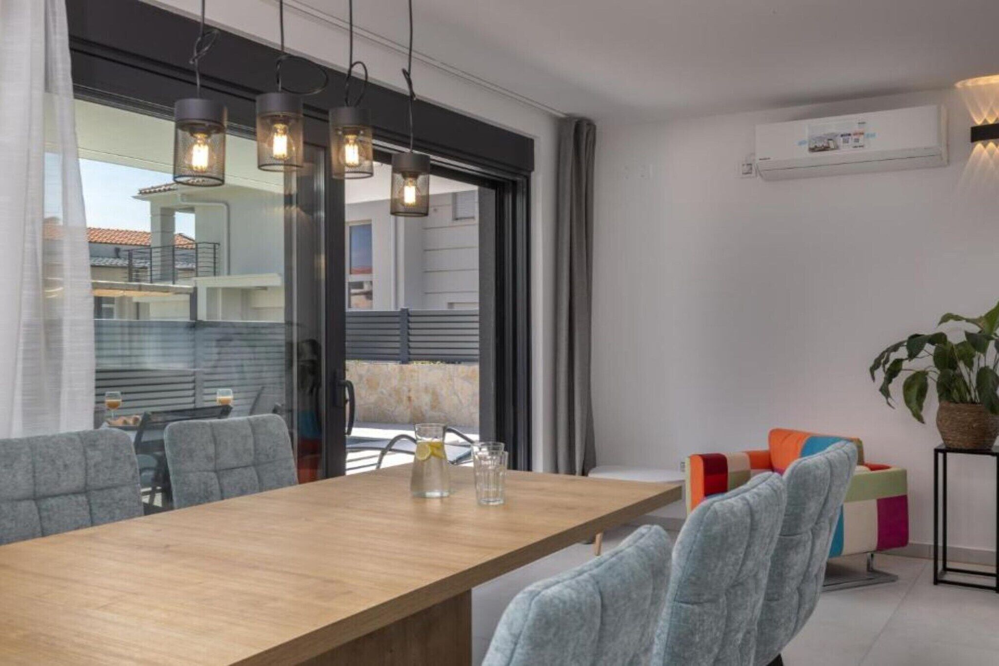 Zona pranzo moderna con tavolo in legno, sedie rivestite in grigio e illuminazione a sospensione.