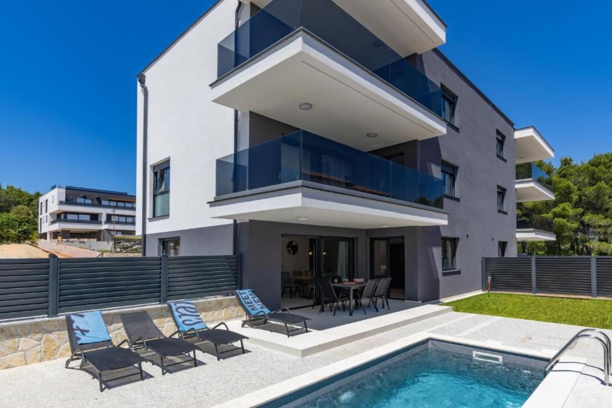 A modern two-story building with a swimming pool, outdoor seating, and a balcony.