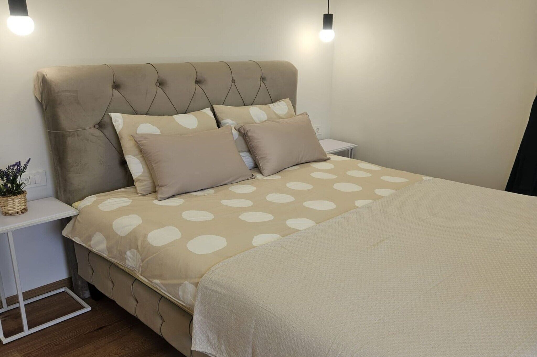 A bedroom with a tufted headboard, a bed with a polka dot bedspread, two bedside tables, and a small potted plant.
