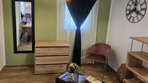 Una habitación con un aparador de madera, un globo en una mesa, una silla rosa, un reloj negro y una ventana con cortinas.