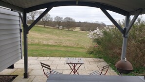 Une terrasse couverte, avec une table et des chaises, donnant sur un champ verdoyant et des arbres.