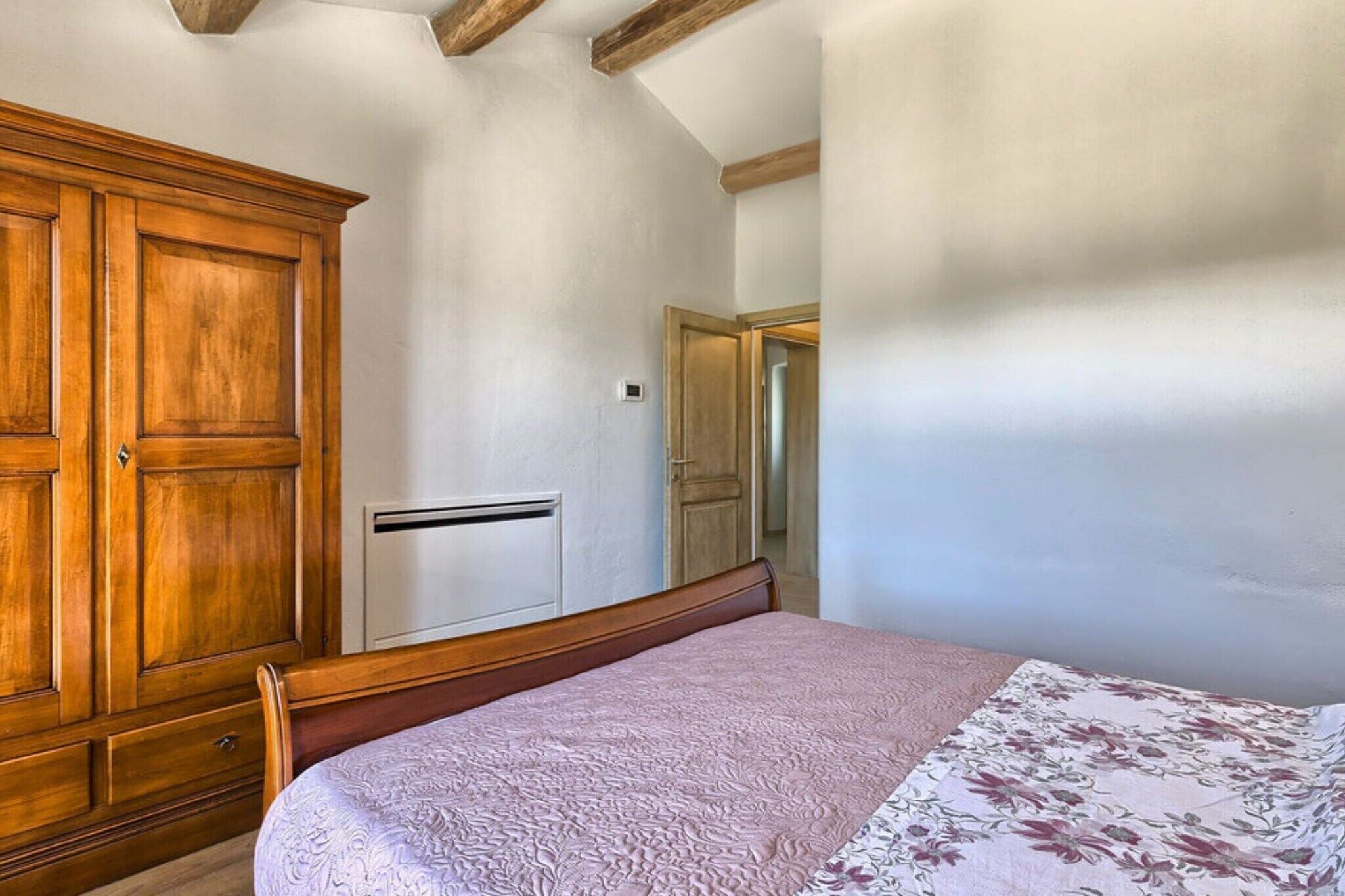 Une chambre avec une armoire en bois, un lit recouvert d’une couvre-lit à motifs floraux et un mur blanc.