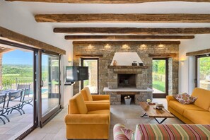Un salon moderne doté d’une cheminée en pierre, de sièges confortables et d’une grande fenêtre donnant sur un paysage pittoresque.