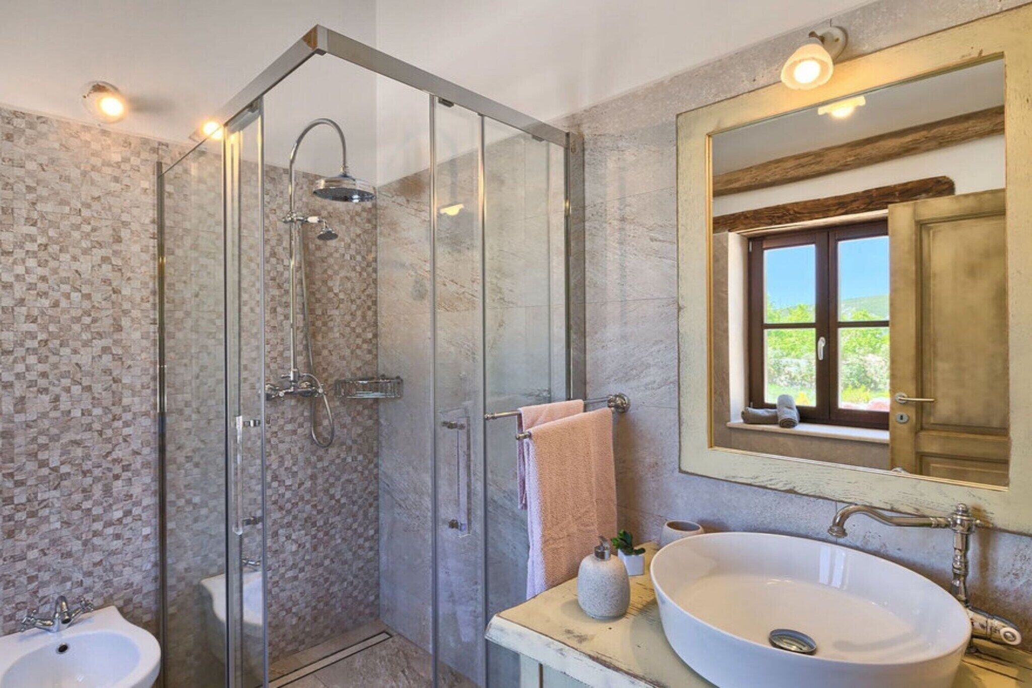 Un baño con ducha acristalada, lavamanos y ventana con vistas.