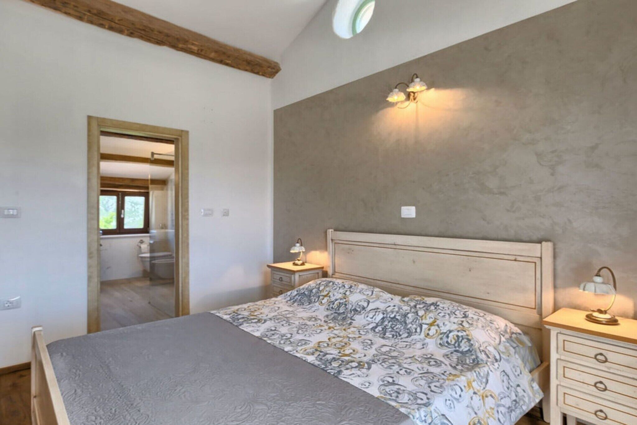 A bedroom with a bed, bedside tables, a wall-mounted light fixture, and a door leading to a bathroom.
