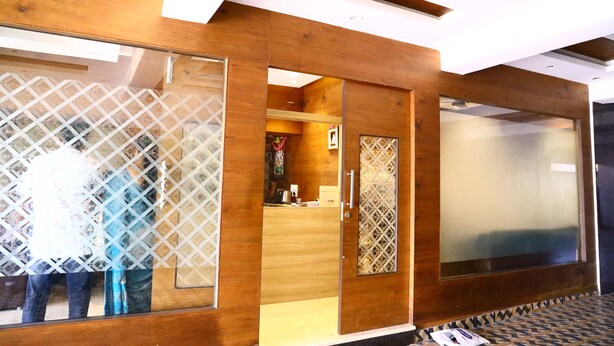 A modern hotel room with wooden paneling, a large window, and a reception area visible through a glass door. - SP Residency (Pollachi)
