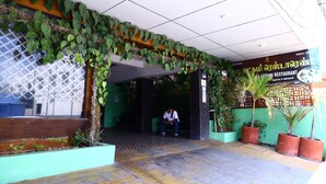 A restaurant entrance with a tiled floor, a man sitting inside, and potted plants. - SP Residency (Pollachi)