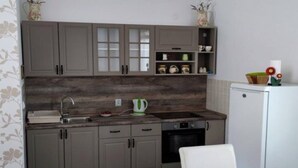 Eine kompakte Küche mit grauen Schränken, einem weißen Kühlschrank und einer kleinen Essecke mit einem weißen Stuhl.