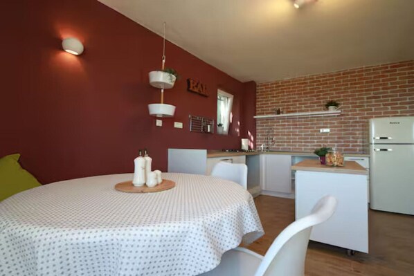 A compact kitchen with a brick wall, a white refrigerator, and a small dining area with a round table and chairs. - Stone House Bay View Kaštela - Two Bedroom House with Pool (Kastel Luksic)