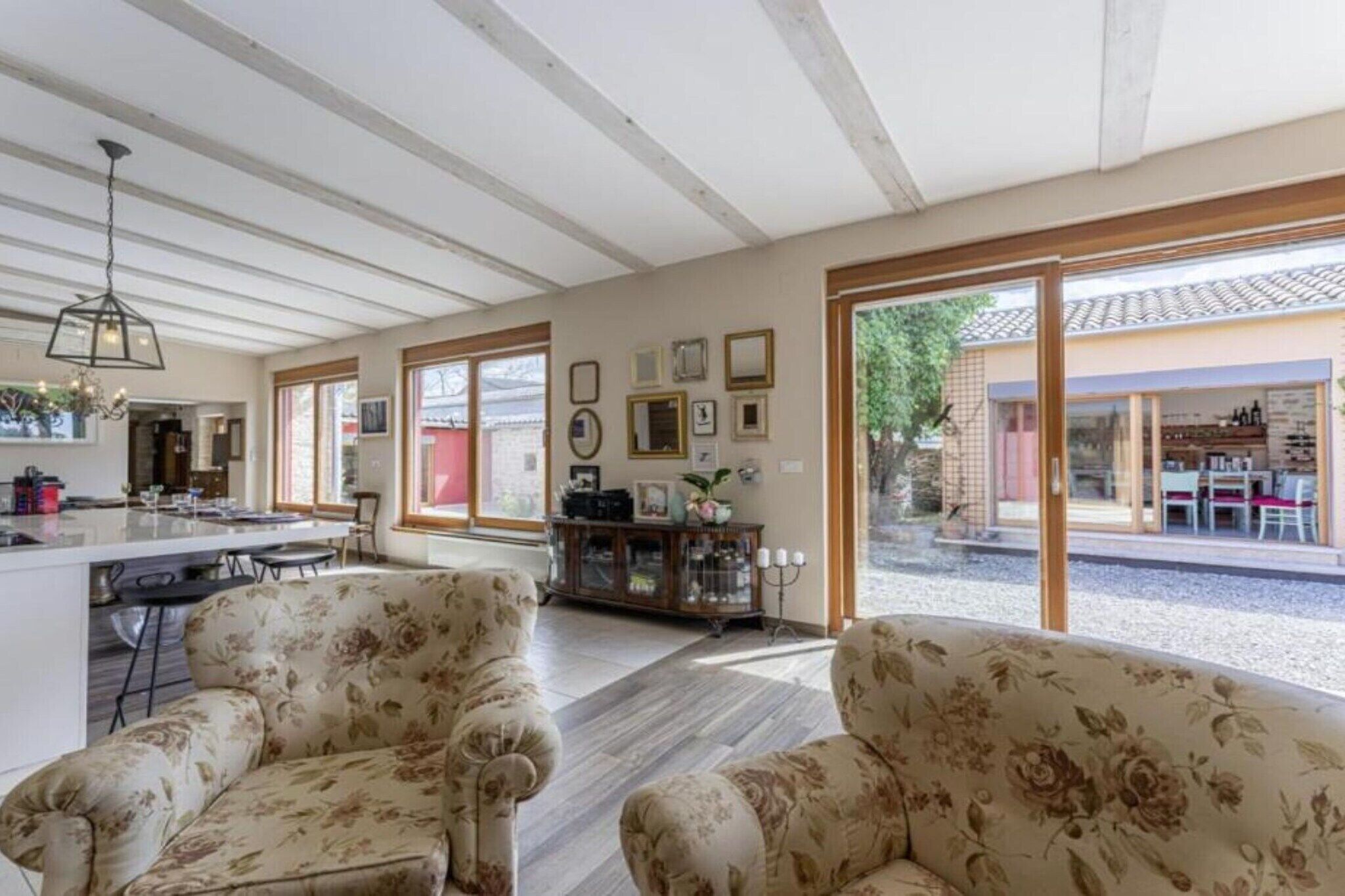 A spacious living area with floral-patterned sofas, a dining table, and a kitchen area with a bar.