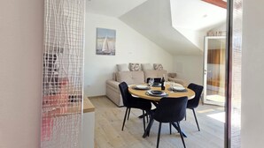 Een eetgedeelte met een ronde tafel, zwarte stoelen en een bank met kussens op de achtergrond.