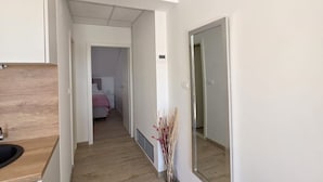 Een hal met een houten vloer, een spiegel aan de rechterkant en een bed op de achtergrond.