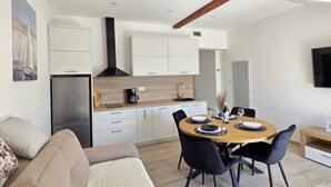 Een moderne keuken met witte kasten, een zwarte afzuigkap en een houten aanrecht. Er is een zithoek met een ronde tafel en zwarte stoelen.
