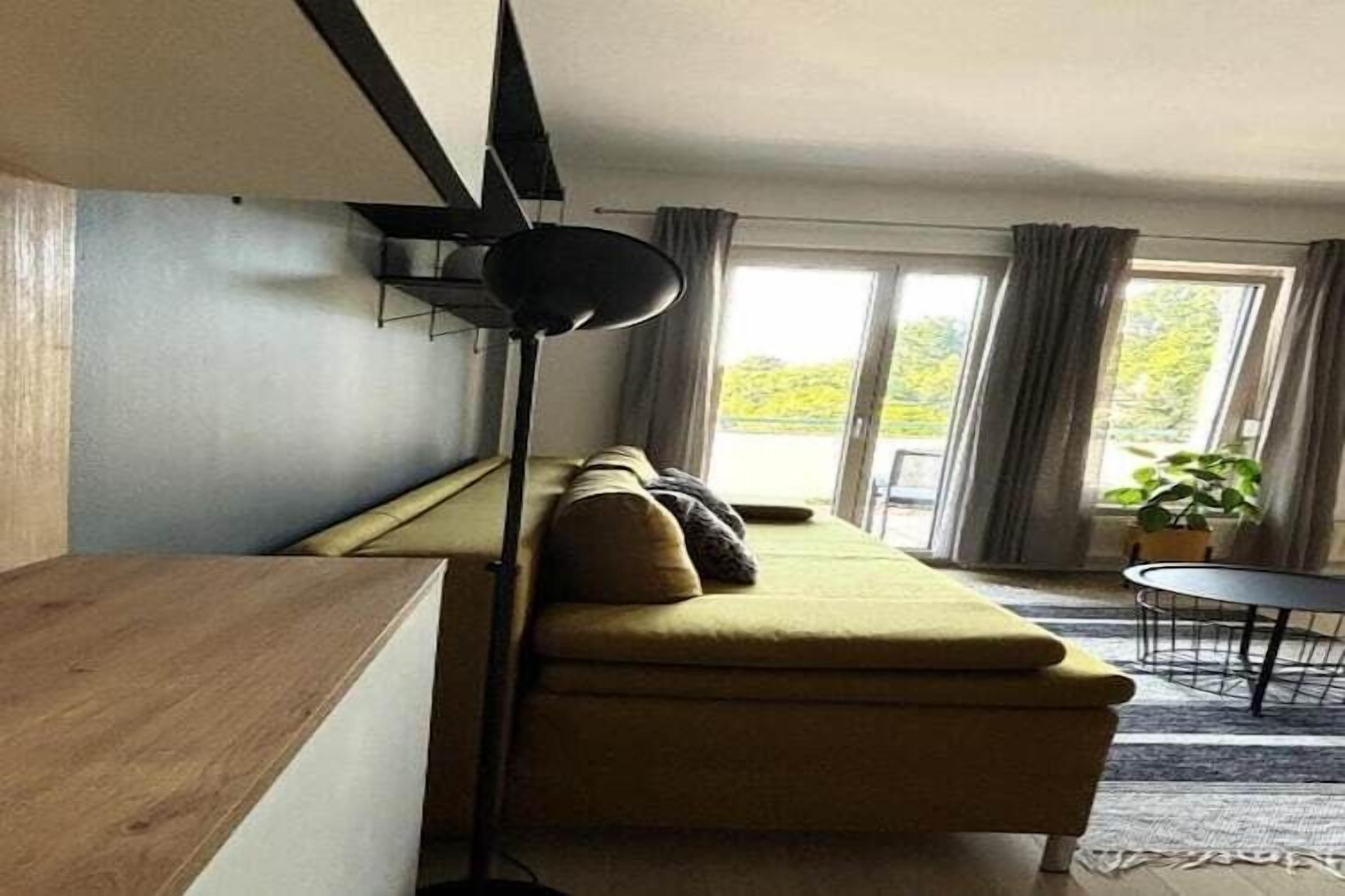 Ein modernes Wohnzimmer mit einer Couch, einer Stehlampe und Blick ins Freie durch ein großes Fenster.
