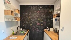 A compact kitchen with a chalkboard wall filled with various writings and drawings, wooden shelves, and a sink. - Modern & Charming - Free Private Parking - One Bedroom Apartment (Zagreb)