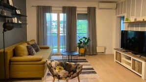 A living room with a sofa, a coffee table, a TV stand, and a large window with curtains. - Modern & Charming - Free Private Parking - One Bedroom Apartment (Zagreb)
