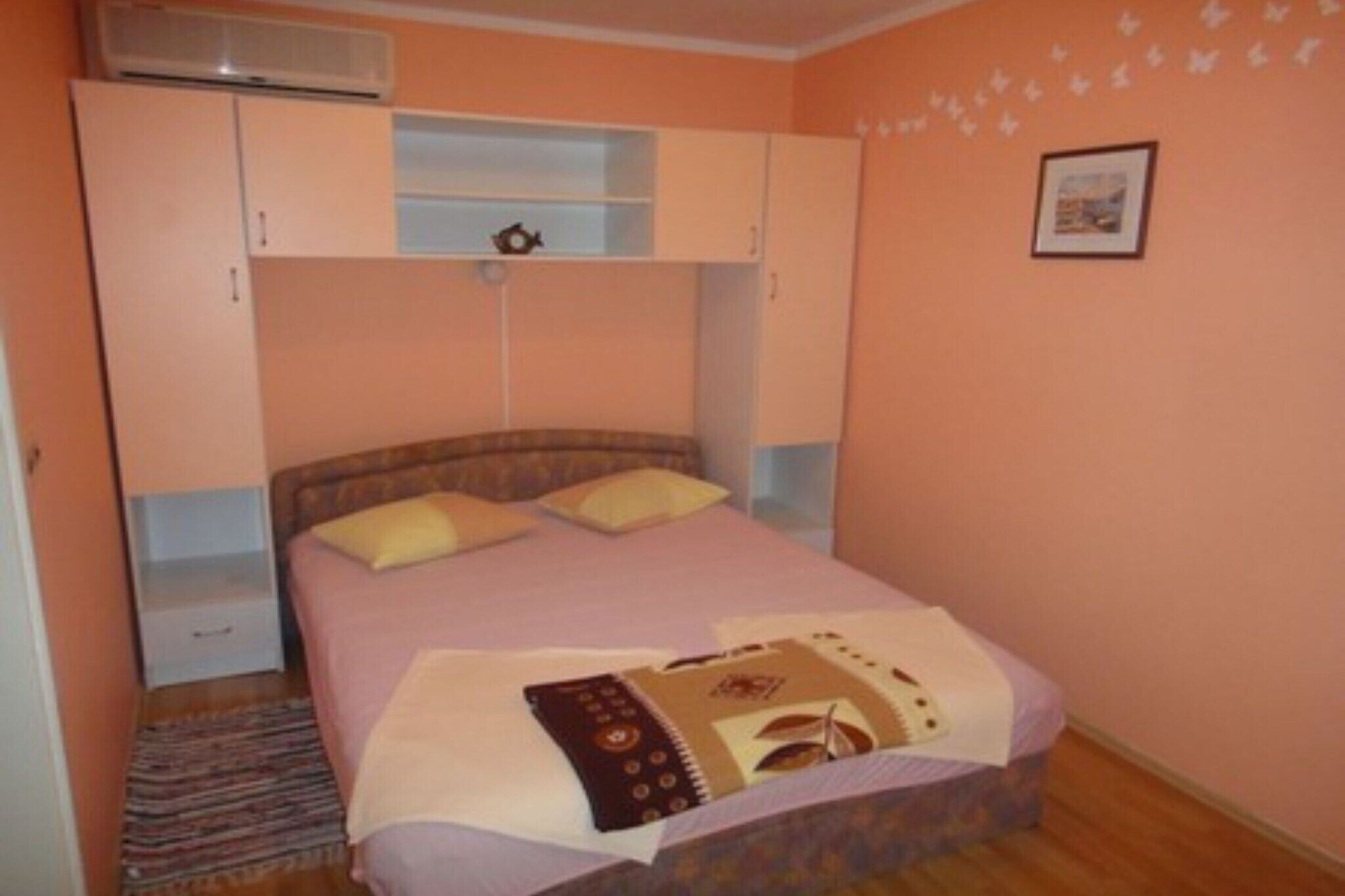 Ein Schlafzimmer mit Bett, Kleiderschrank, einem kleinen Tisch und einem Wandheizgerät.
