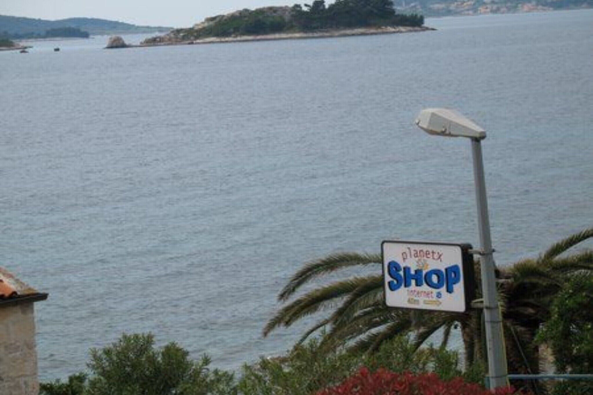 A sign for 'planetx shop' near a body of water with a view of the sea and distant land.