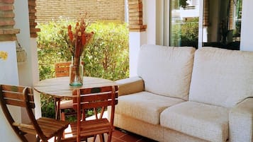 Une terrasse avec un canapé beige, des chaises en bois et une petite table sur laquelle est posé un vase rempli de fleurs séchées.