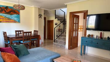 Un salon avec un canapé, une table à manger et des chaises, un escalier et un téléviseur.