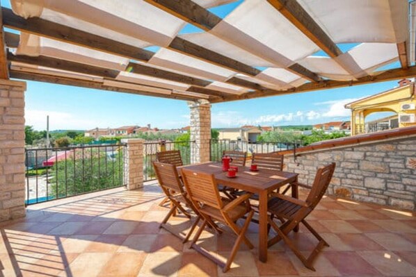 Um pátio externo com mesa, cadeiras, paredes de pedra e vista para a paisagem ao redor.