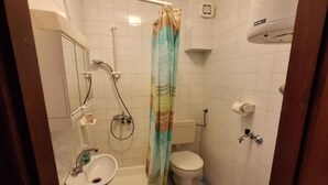 Pieni kylpyhuone, jossa on suihku, wc, pesuallas ja peili.