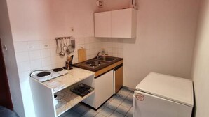 Pieni, käytännöllinen keittiö, jossa on liesi, pesuallas ja valkoiset kaapit.