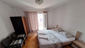 Un dormitorio con una cama, dos sillas, suelo de madera, una ventana con cortinas y un ventilador de techo.