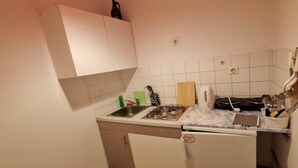 Cocina compacta con estufa a gas, lavamanos y armarios blancos.