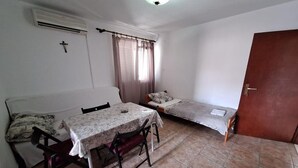 Un alojamiento pequeño de una sola habitación, con cama, mesa y sillas, ventana con cortinas y puerta.