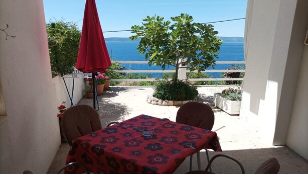 A balcony with a table and chairs, a red umbrella, and a view of the sea. - Sea View Apartments Lendic Podgora - Comfort Studio Apartment with  Balcony and Sea View (Podgora)