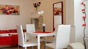 A dining area with a white table and chairs, a red placemat, and a vase with white flowers. There is a painting of flowers on the wall and a mirror with a red frame. - Sea View Apartments Lendic Podgora - Comfort Studio Apartment with  Balcony and Sea View (Podgora)