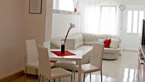 A modern living room with a white sofa, a dining table with chairs, and a red placemat. - Sea View Apartments Lendic Podgora - Comfort Studio Apartment with  Balcony and Sea View (Podgora)