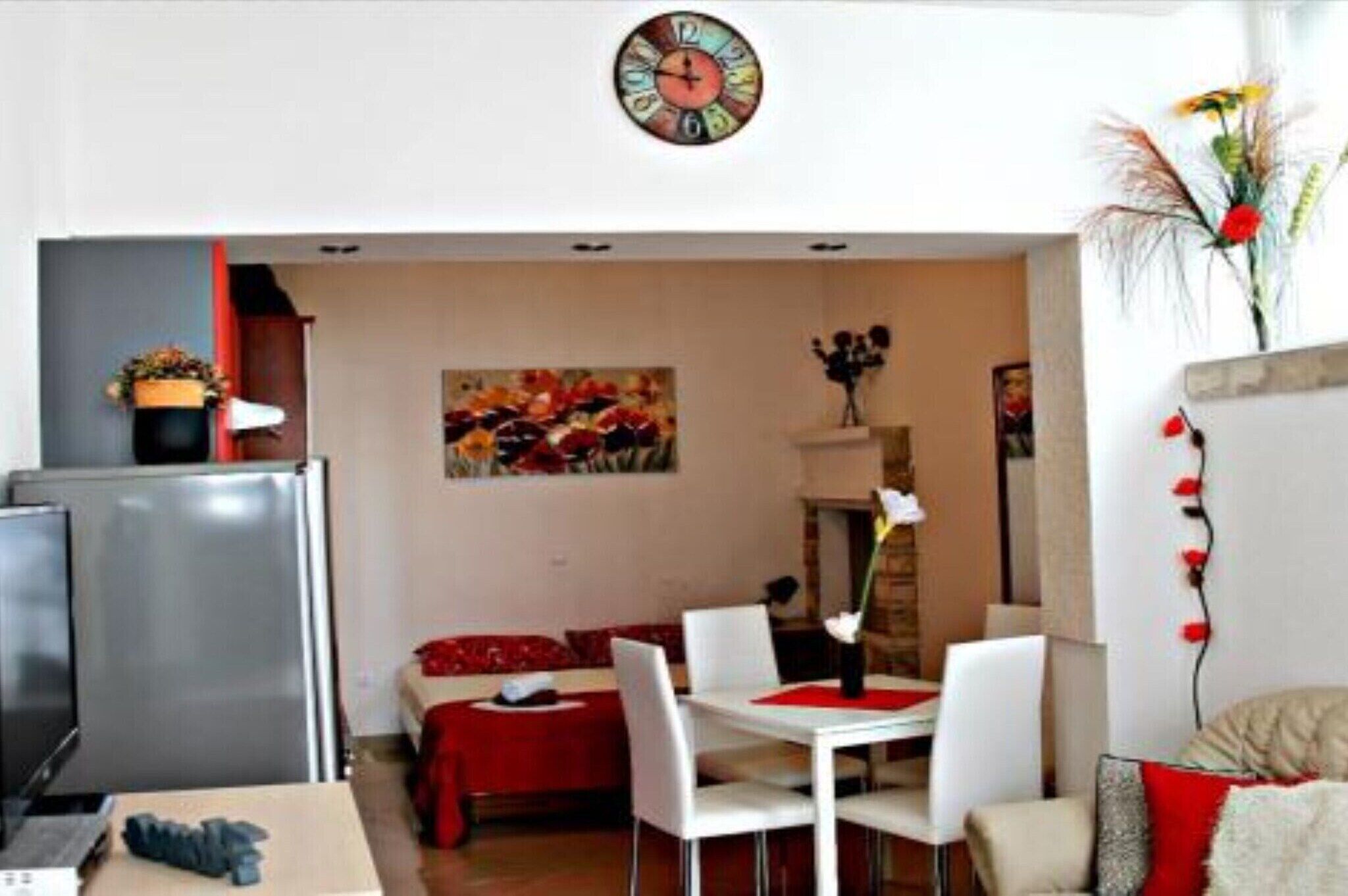 Un'area pranzo con tavolo e sedie bianche, tovaglia rossa e un orologio appeso al muro.