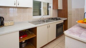 A kitchen with white cabinets, a sink, a stove, and a window with blinds. - Sea View Apartments Lendic Podgora - Classic Studio Apartment with Terrace and Sea View (Podgora)